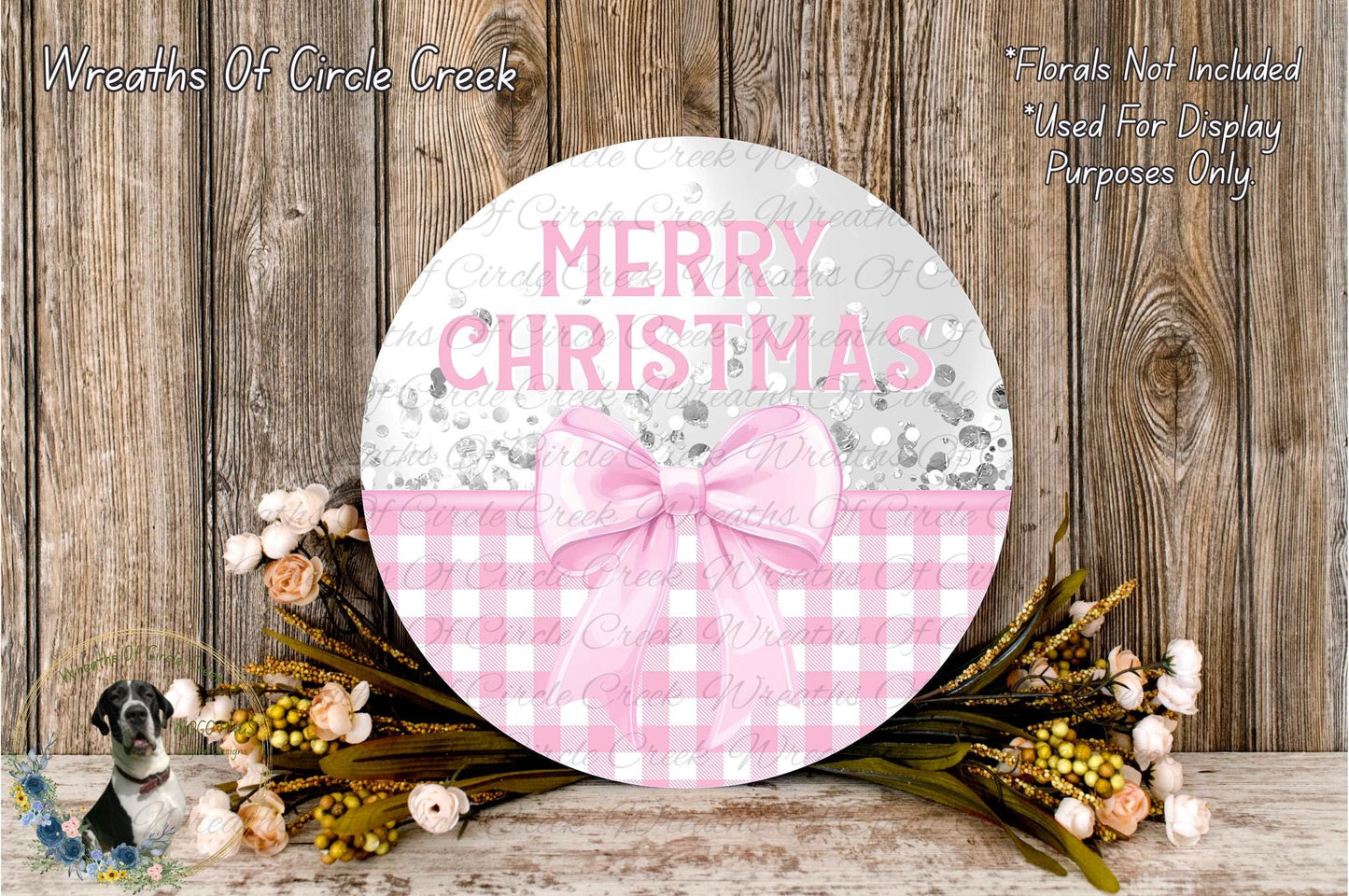 a round wooden sign with the text "MERRY CHRISTMAS" and a pink bow, surrounded by a floral arrangement and a wooden background.