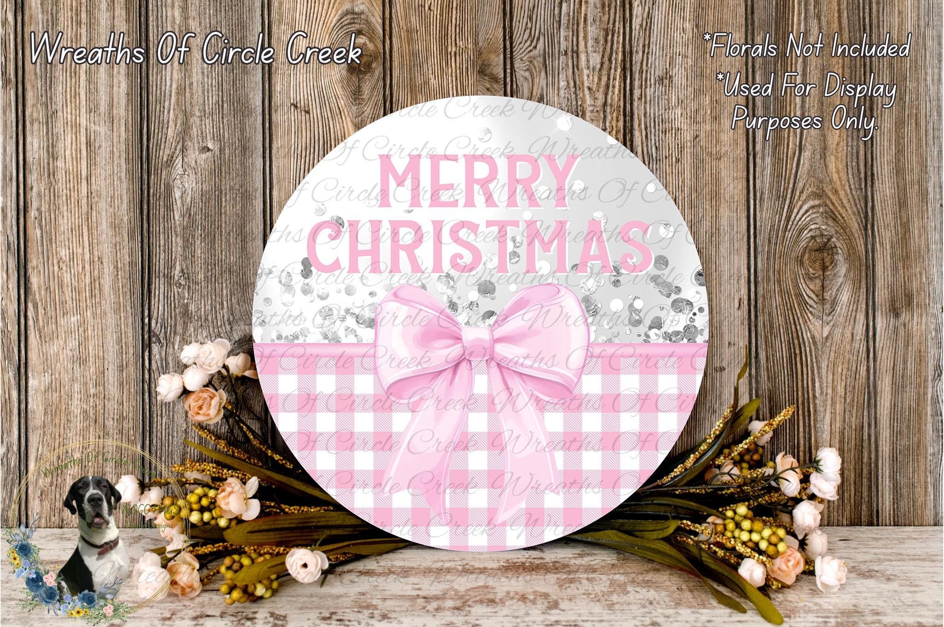 a round wooden sign with the text "MERRY CHRISTMAS" and a pink bow, surrounded by a floral arrangement and a wooden background.