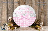 a round wooden sign with the text "MERRY CHRISTMAS" and a pink bow, surrounded by a floral arrangement and a wooden background.