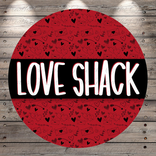 A circular red background with the word "LOVE SHACK" written in bold white letters. The background has a repeating pattern of hearts and arrows, creating a festive and celebratory design.