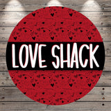 A circular red background with the word "LOVE SHACK" written in bold white letters. The background has a repeating pattern of hearts and arrows, creating a festive and celebratory design.