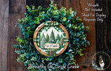 A wreath made of evergreen branches and a sign that says "Let it snow" is displayed on a wooden surface.