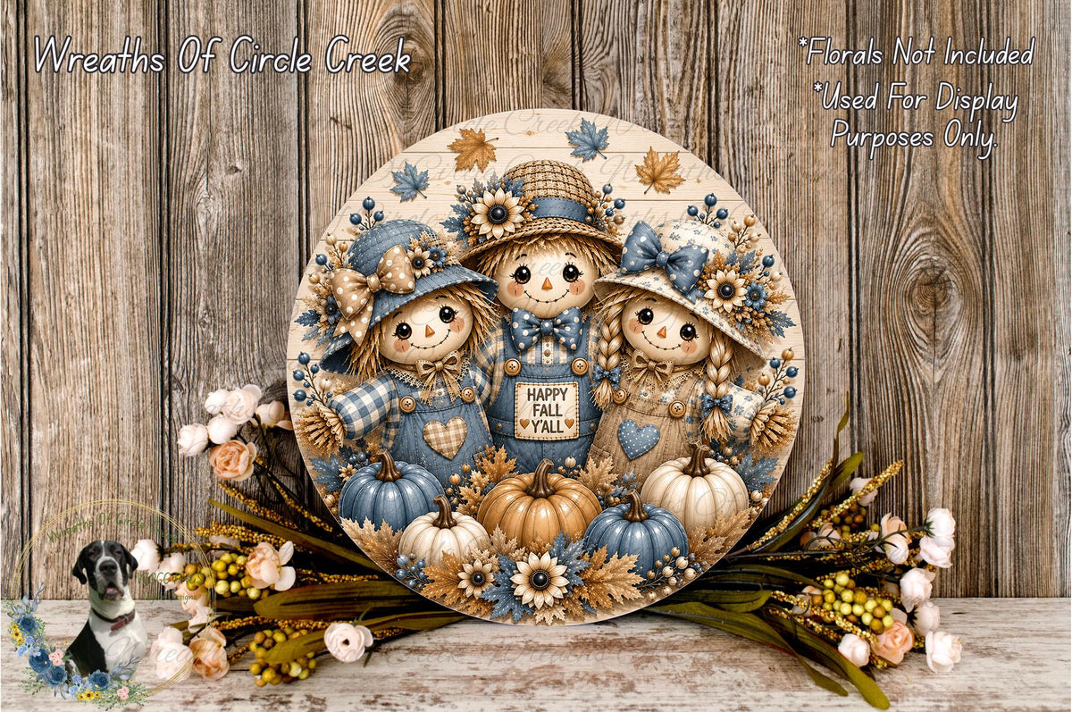 A decorative wreath featuring three scarecrow figures surrounded by autumn-themed elements such as pumpkins, flowers, and leaves. The wreath is displayed on a wooden surface, with a floral arrangement and a small bird figurine nearby.