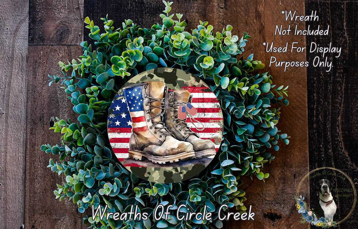 A wreath made of green foliage and a pair of worn boots, with an American flag design, is displayed on a wooden surface.
