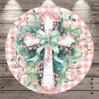 A circular, decorative image featuring a white cross adorned with pink flowers and leaves, surrounded by green vines and leaves, all set against a pink and white checkered background.