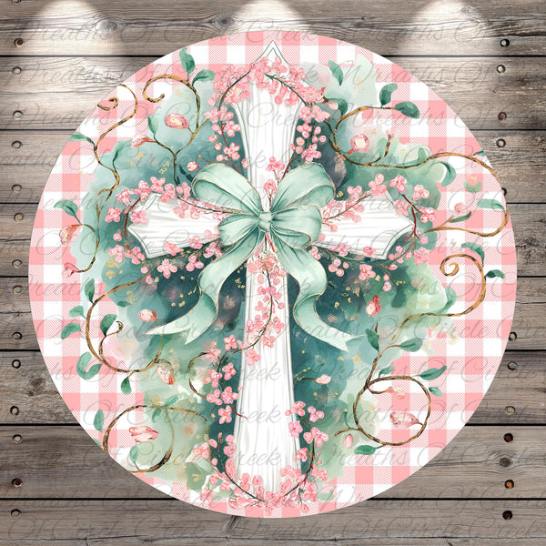 A circular, decorative image featuring a white cross adorned with pink flowers and leaves, surrounded by green vines and leaves, all set against a pink and white checkered background.