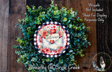 a wreath made of various green plants and flowers, with a decorative envelope and a welcome sign in the center. The wreath is displayed on a wooden surface, and there is a text overlay that reads "Welcome Wreath Not Included * Used For Display Purposes Only".