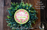a wreath made of various green and pink flowers, with a circular sign in the center that reads "Welcome to our home".