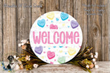 a round sign with the word "WELCOME" written on it, surrounded by various heart-shaped candies and flowers.