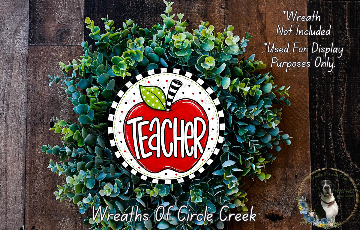A wreath made of green leaves and a red apple with the word "Teacher" written on it, placed on a wooden surface.