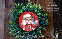 A wreath featuring a Santa Claus figure holding a gift box, surrounded by a lush green plant.