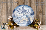 a round sign with a winter village scene, surrounded by flowers and placed on a wooden surface.