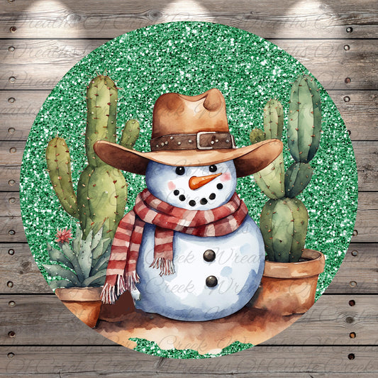A snowman wearing a cowboy hat and scarf, surrounded by cacti, is depicted in a circular frame with a glittery green background.