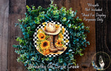 A wreath made of green foliage and yellow sunflowers, with a cowboy hat and boots placed in the center.