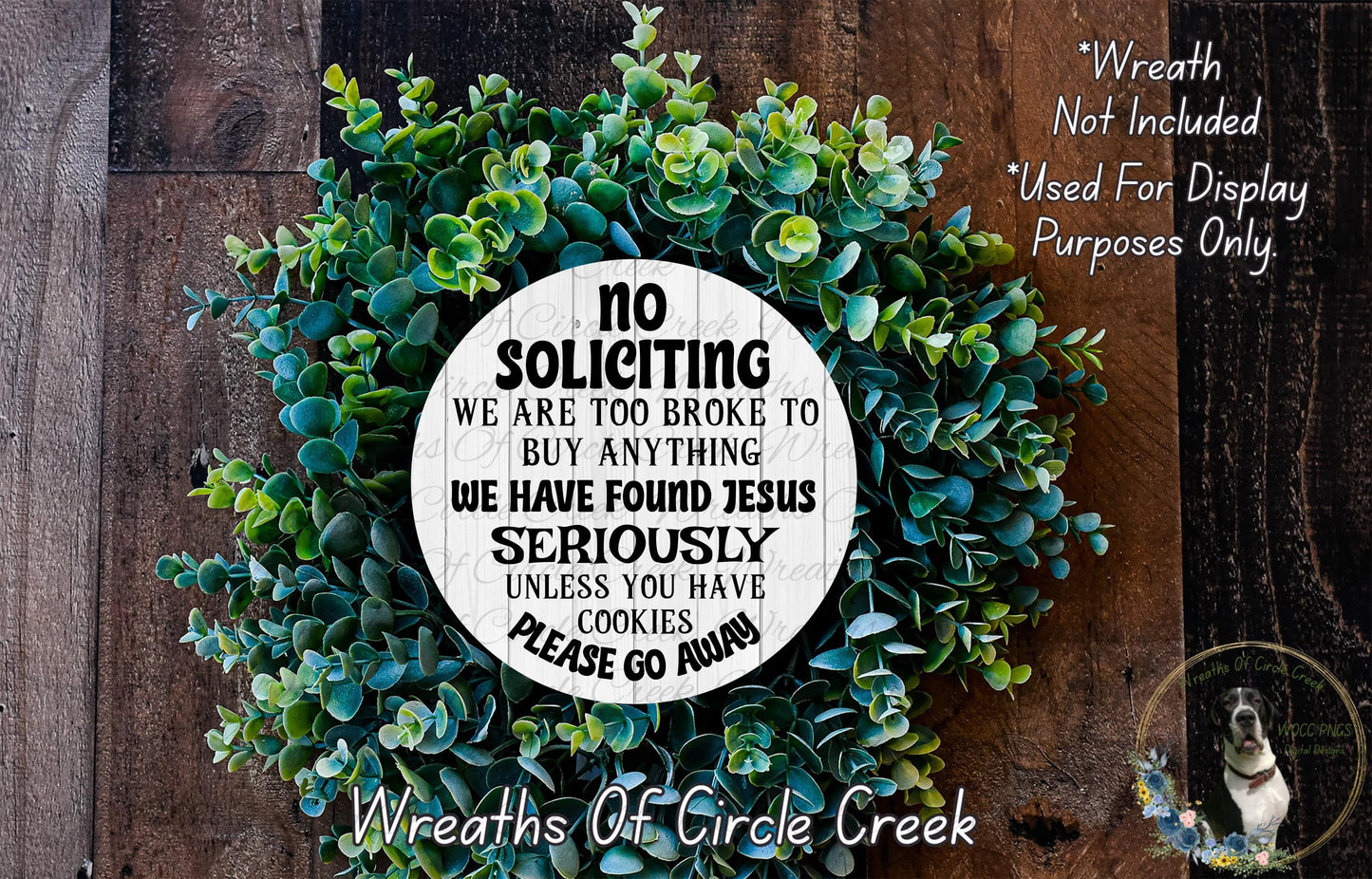 a wreath made of green leaves and a white sign with text on it, placed on a wooden surface.