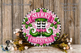 A festive Christmas wreath with the text "MERRY CHRISTMAS" displayed prominently. The wreath is adorned with green elf-like feet, a pink banner, and various holiday-themed elements such as flowers and leaves. The wreath is set against a rustic wooden background, creating a warm and inviting holiday atmosphere.