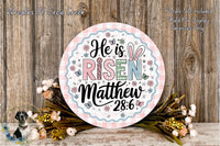 a decorative Easter-themed sign with the text &quot;He is risen Matthew 28:6&quot; surrounded by a floral arrangement and a wooden background.