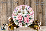 a round floral wreath with a cross and pink roses, surrounded by various flowers and greenery, placed on a wooden surface.