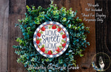 a wreath made of various green plants and a circular sign with the text "Home Sweet Home" on it. The sign is surrounded by a lush, colorful wreath.