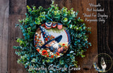 A wreath made of green leaves and flowers, featuring a painted image of a gnome wearing a hat and holding a flag.