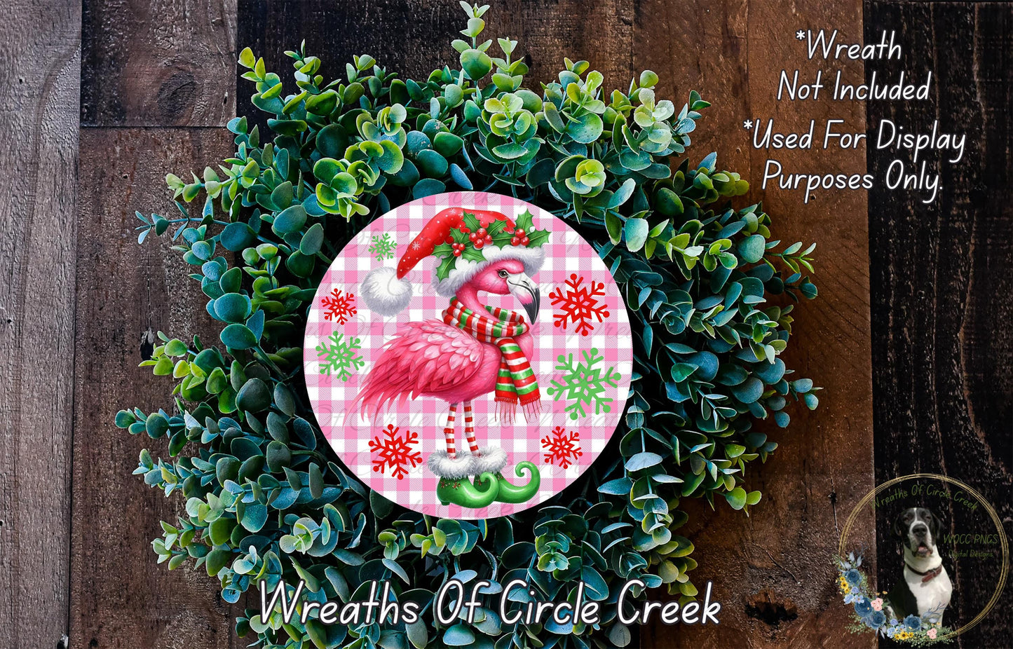 A wreath made of green foliage and featuring a pink flamingo wearing a Santa hat and scarf.