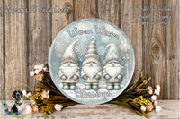 A round decorative plate featuring three gnomes wearing winter hats and scarves, surrounded by a floral arrangement and a wooden background.