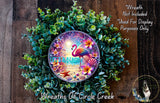 A wreath made of various green plants and flowers, with a large circular design in the center featuring a flamingo and a beach scene.