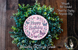 A wreath made of green leaves and flowers, with a pink circular sign that says "Happy Birthday Girl" surrounded by butterflies.