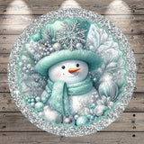 A snowman wearing a green hat and scarf, surrounded by snowflakes, pine branches, and ornaments, is the central focus of the image.