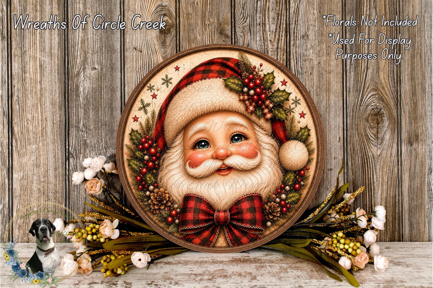 A decorative wreath featuring a painted Santa Claus face surrounded by pine cones, berries, and greenery, placed on a wooden surface.