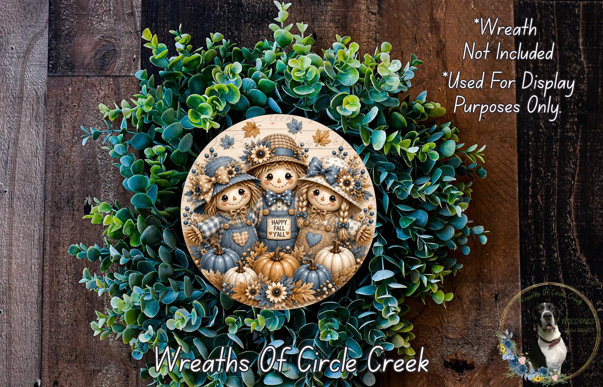 a wreath with a central design of three scarecrow figures, surrounded by a lush green wreath. The wreath is displayed on a wooden surface, and there is a small dog visible in the bottom right corner of the image.