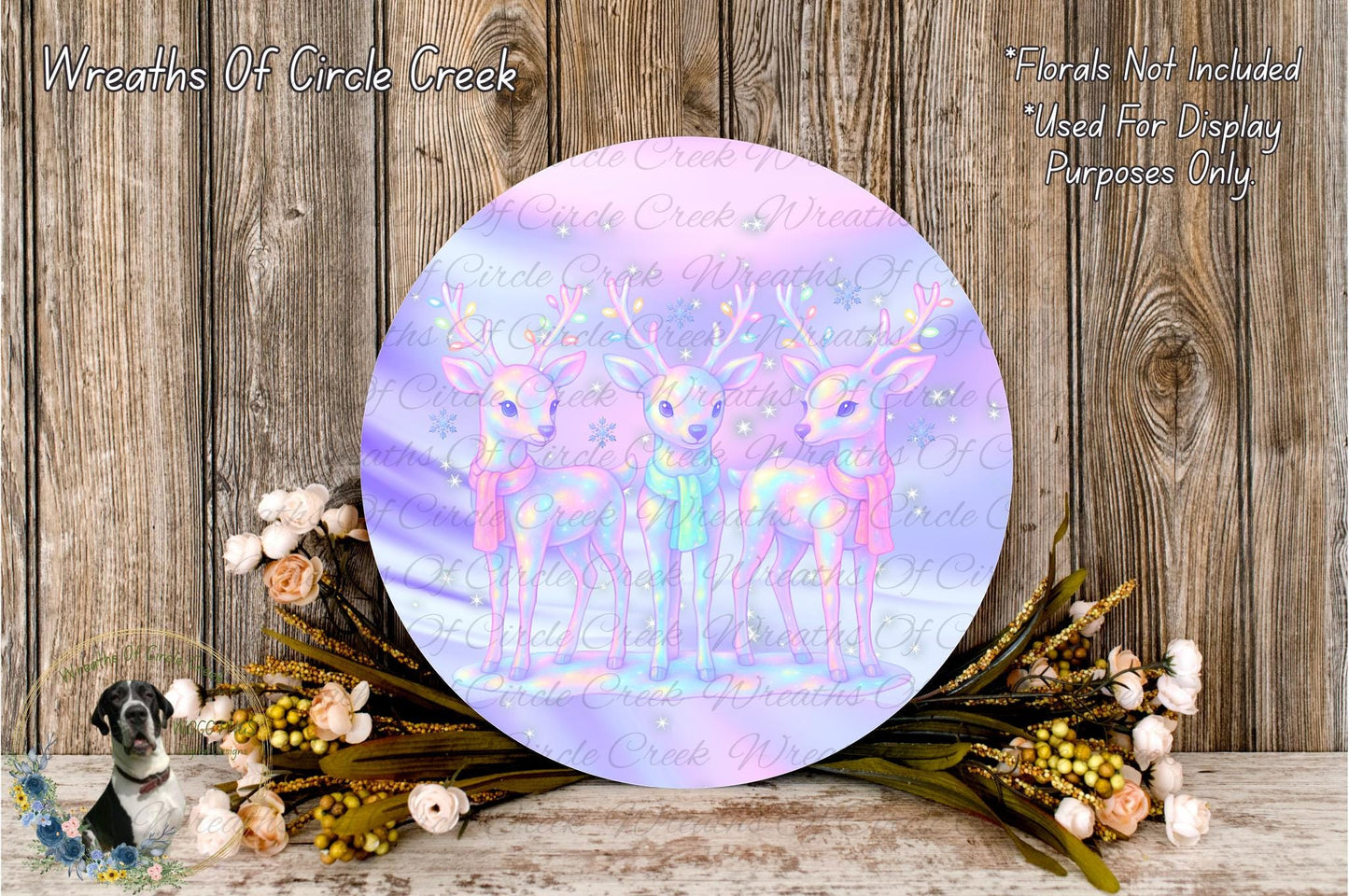 a circular wreath with three deer on it, surrounded by flowers and placed on a wooden surface.