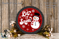 A decorative snowman sign with the text "Let It Snow" is displayed on a wooden surface, surrounded by flowers and greenery.