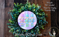 A wreath made of green leaves and a circular design featuring three nutcracker figurines in different colored outfits.