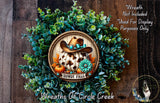a wreath with a cowboy hat and a pumpkin, surrounded by greenery and a wooden background.