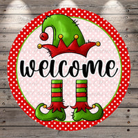 A circular sign featuring a green elf hat, red and green striped boots, and the word "welcome" written in a cursive font.