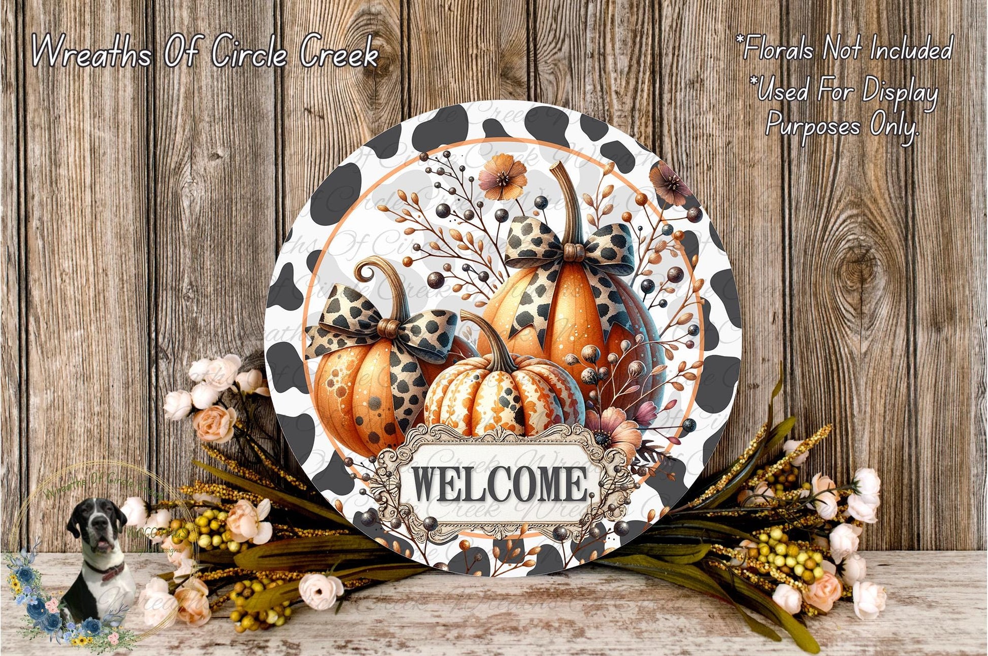 a decorative welcome sign with a floral design, surrounded by a wreath of flowers and autumn foliage. The sign displays the word "WELCOME" and includes two decorative pumpkins with bows. The background is a wooden wall with a rustic, natural appearance.