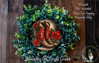 A wreath made of green foliage and red poinsettia flowers, with a pair of red cowboy boots placed in the center.