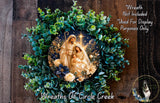 A wreath with a nativity scene featuring the Virgin Mary, baby Jesus, and the baby Jesus' parents. The wreath is surrounded by greenery and flowers, creating a festive and decorative arrangement.