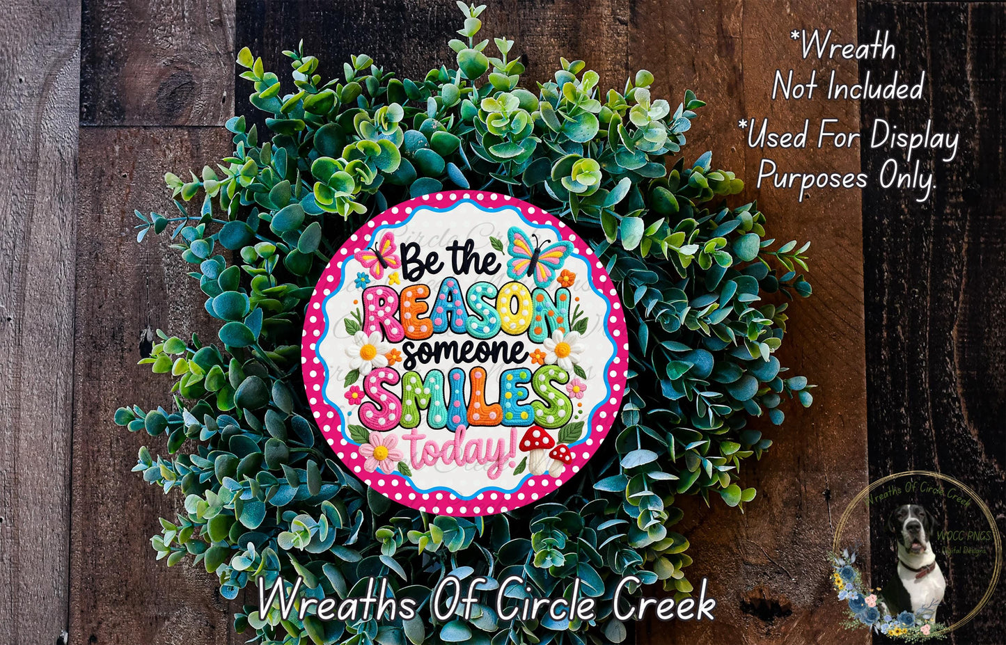 a wreath made of green leaves and flowers, with a colorful sign that reads "Be the reason someone smiles today".