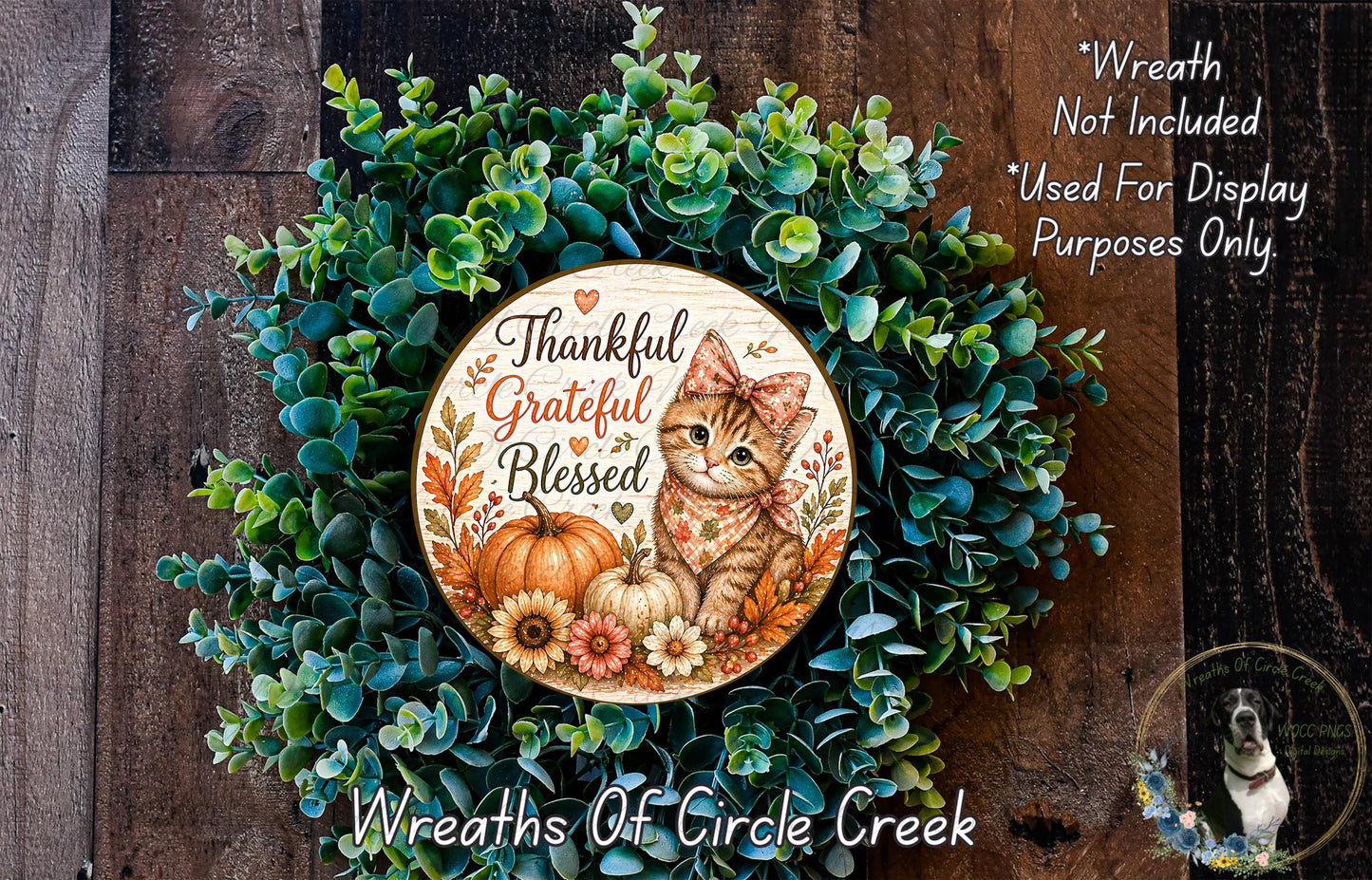 A wreath made of green leaves and flowers, with a wooden sign featuring a cat and a pumpkin, placed on a wooden surface.