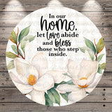 The image is a circular graphic with a floral design and text. The text reads, "In our home, let love abide and Bless those who step inside."