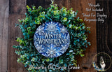 A wreath made of green leaves and blue snowflakes, with the text "Winter Wonderland" displayed on it. The wreath is placed on a wooden surface, and there is a small dog in the bottom right corner of the image.