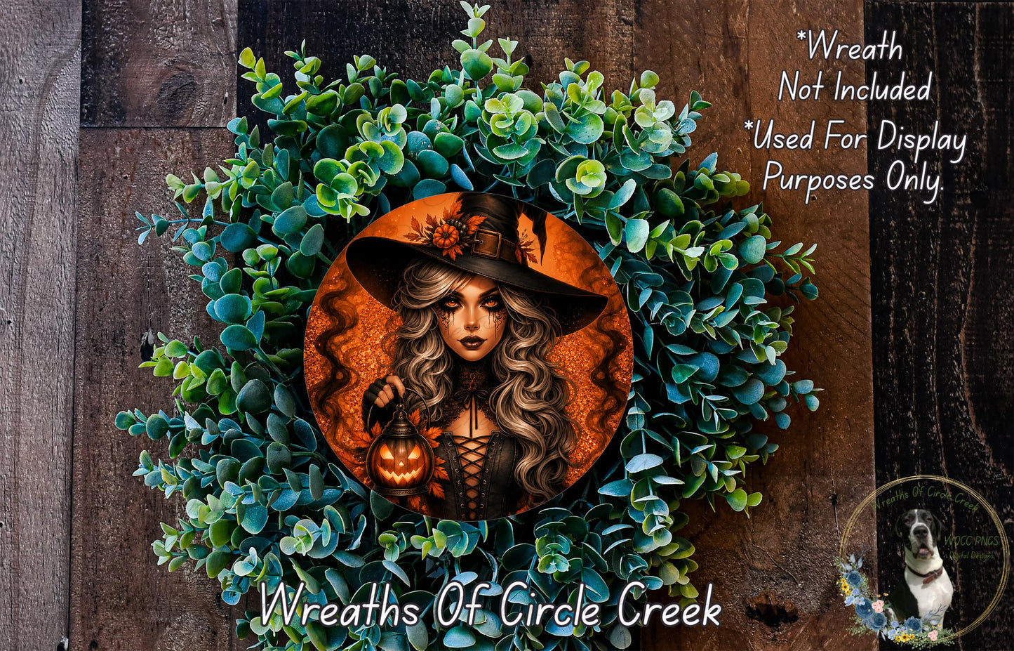 a wreath with a woman wearing a witch's hat and holding a lantern, surrounded by green foliage.