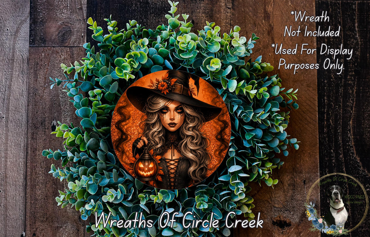 a wreath with a woman wearing a witch's hat and holding a lantern, surrounded by green foliage.
