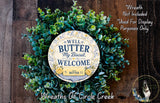 a wreath made of green leaves and a circular sign with text, placed on a wooden surface.