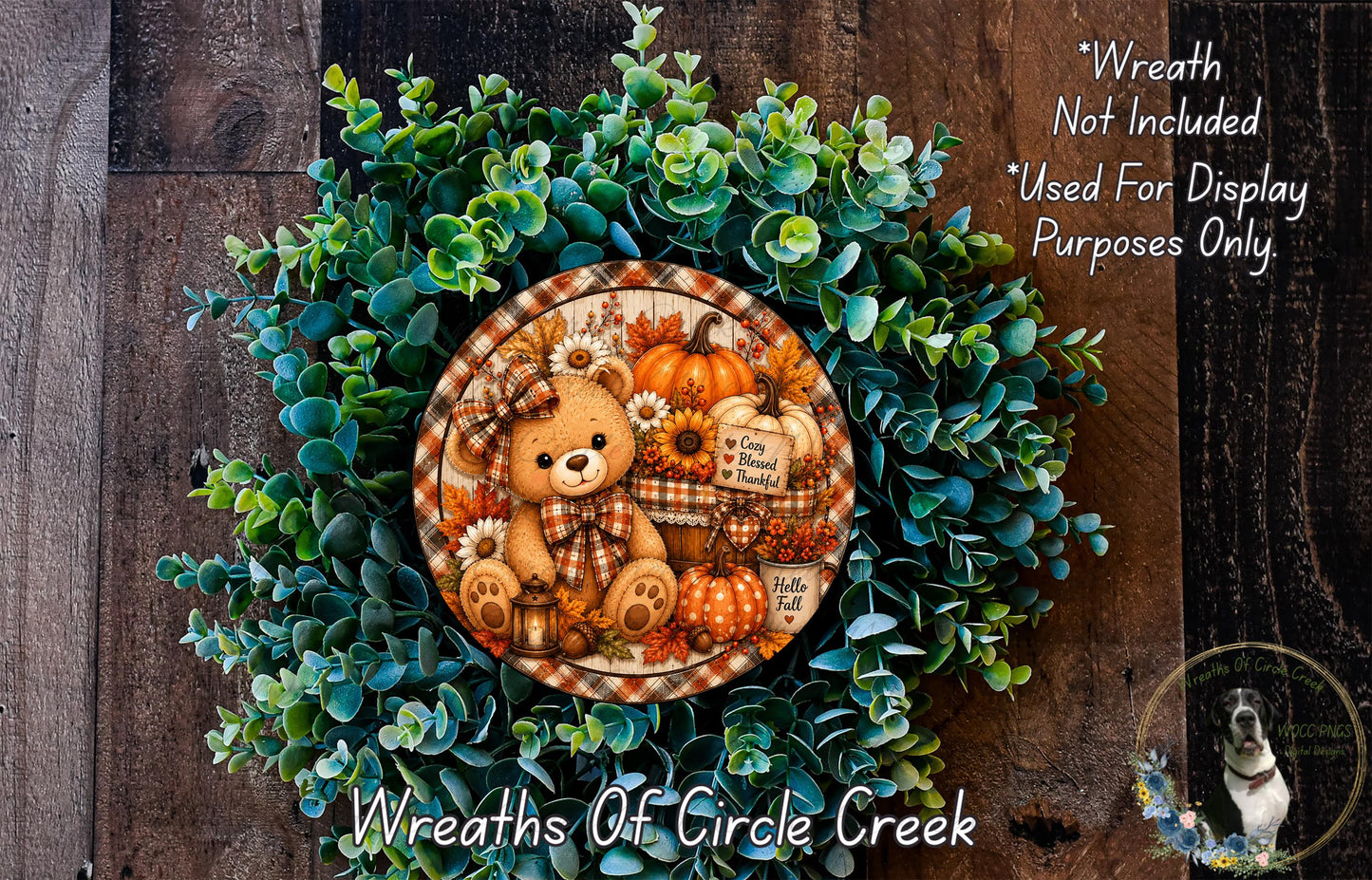 A wreath made of green leaves and orange pumpkins, featuring a teddy bear and other fall-themed decorations.