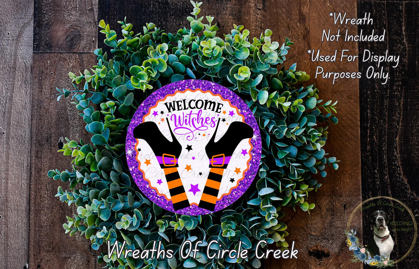 a wreath made of green leaves and purple glitter, with a sign that reads "Welcome Witches" in the center. The wreath is displayed on a wooden surface, and there is a small dog in the bottom right corner.