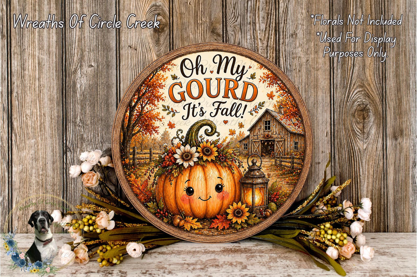 A decorative round sign with a pumpkin and autumn foliage, surrounded by flowers, placed on a wooden surface.