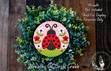 A wreath made of green foliage and flowers, with a red and black ladybug design in the center.